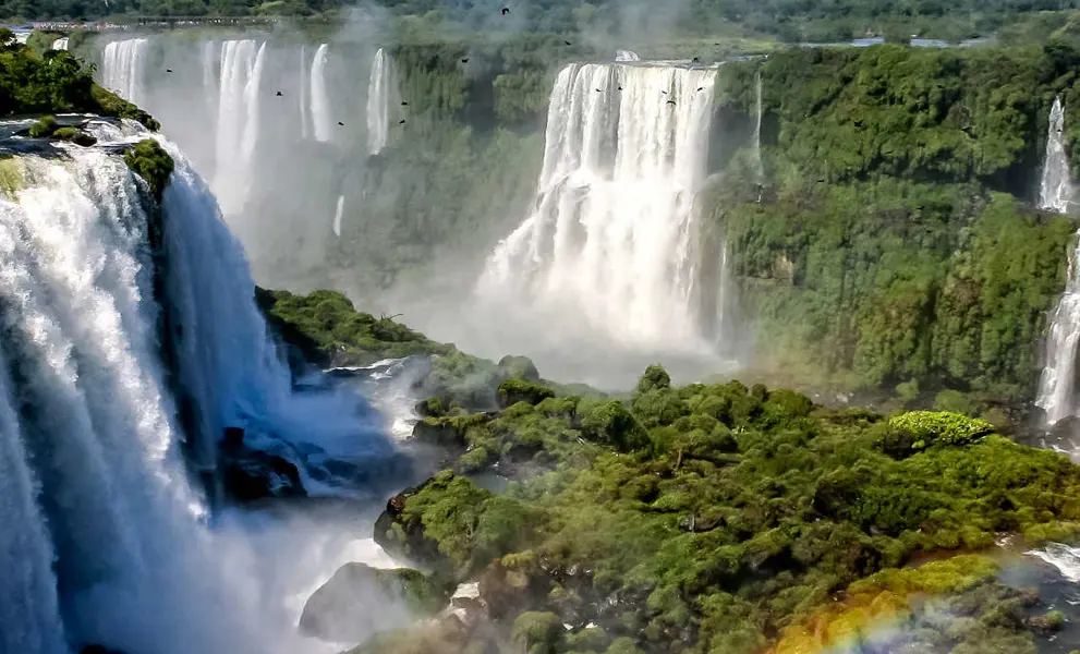Water cascading over the Iguacu falls with rainbow in foreground in Brazil